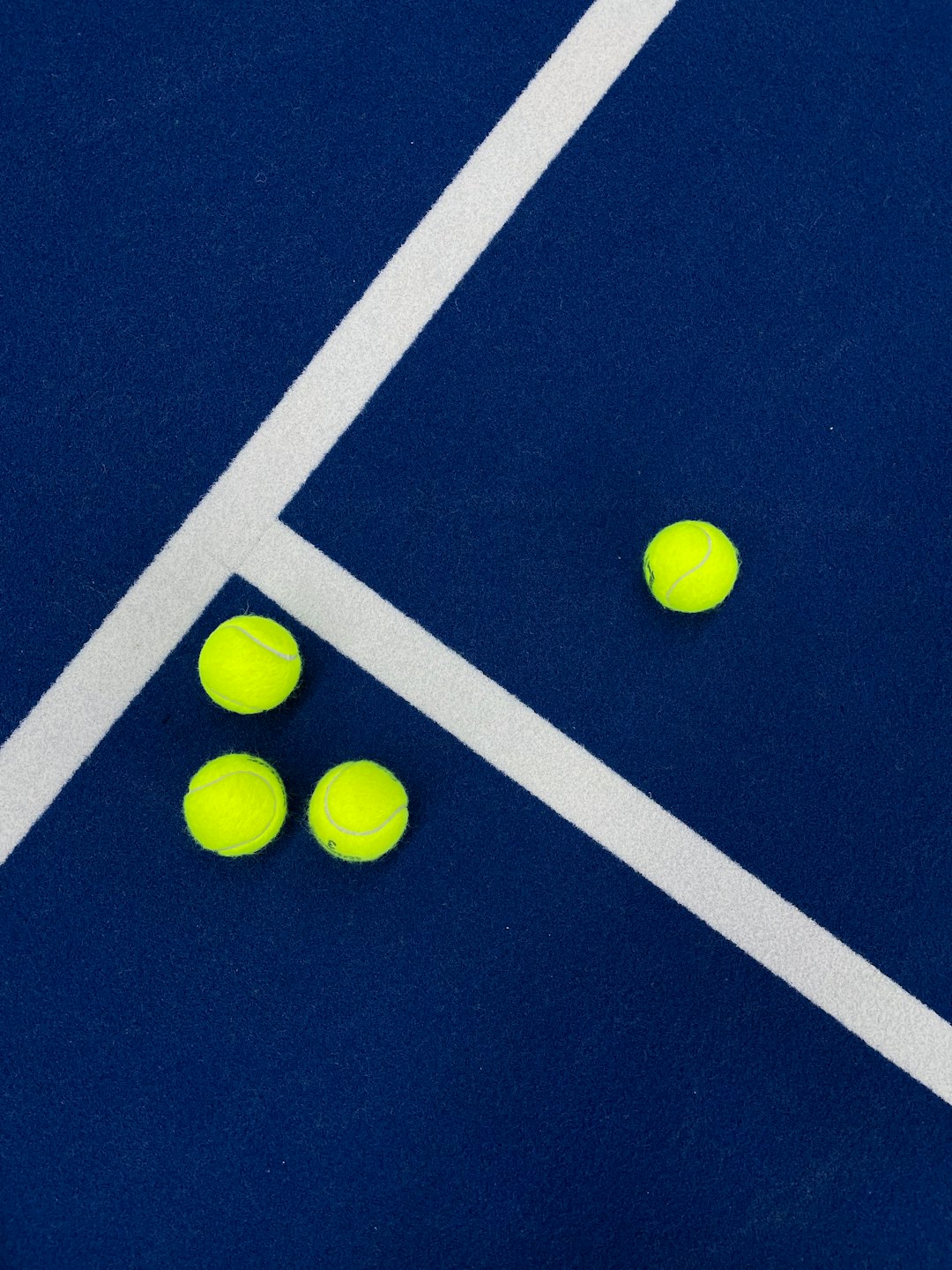 three-tennis-balls-on-a-blue-court-with-white-lines-smv2nshira4